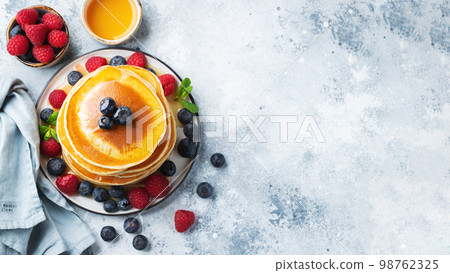 Delicious pancakes, with fresh blueberries, raspberry and maple syrup or honey on a dark background 98762325