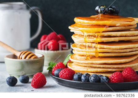 Delicious pancakes, with fresh blueberries, raspberry and maple syrup or honey on a dark background 98762336