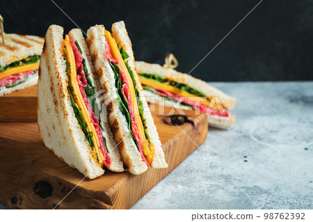 Two homemade sandwiches with sausage, cheese and arugula on a light concrete background Two homemade sandwiches with sausage, cheese and arugula on a light concrete background 98762392