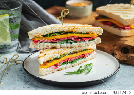 Two homemade sandwiches with sausage, cheese and arugula on a light concrete background Two homemade sandwiches with sausage, cheese and arugula on a light concrete background 98762400