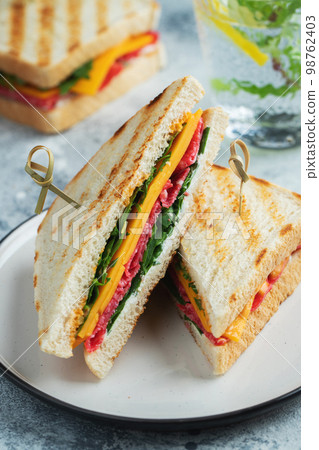 Two homemade sandwiches with sausage, cheese and arugula on a light concrete background 98762403