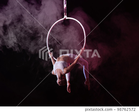 Young woman performing acrobatic element on aerial ring indoors 98762572