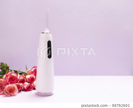 Dental discount, sale. holiday concept. Oral teeth irrigator, roses on purple background. Water tooth cleaner, white portable rechargeable cordless water dental flosser. Home dental care device 98762601