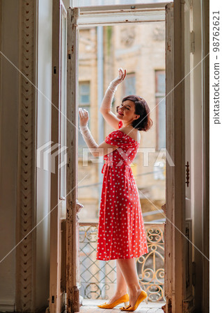 a beautiful and happy brunette women in red retro dress in the balcony doorway  98762621