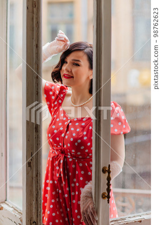a beautiful and happy brunette women in red retro dress in the balcony doorway  98762623