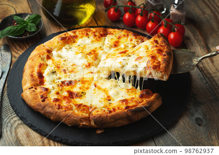 A slice of hot Italian pizza with stretching cheese. Pizza four cheeses with basil. 98762937