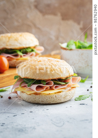 Two homemade sandwiches with ham, cheese and arugula on a concrete table. 98762940