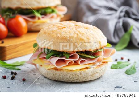 Two homemade sandwiches with ham, cheese and arugula on a concrete table. 98762941