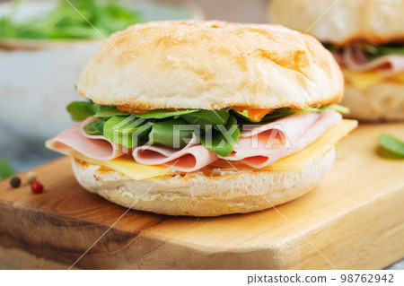 Two homemade sandwiches with ham, cheese and arugula on a concrete table. 98762942