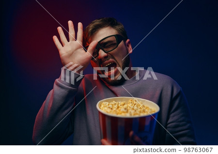 A man is watching a scary movie. Watching a movie with popcorn. 98763067