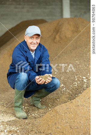 Joyful man farmer at heap of rapeseed oil cake, animal food 98764863
