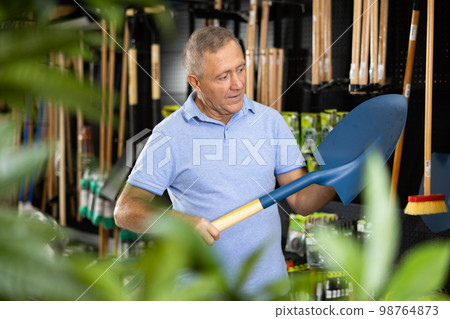Elderly farmer choosing shovel in garden store Elderly farmer choosing shovel in garden store 98764873