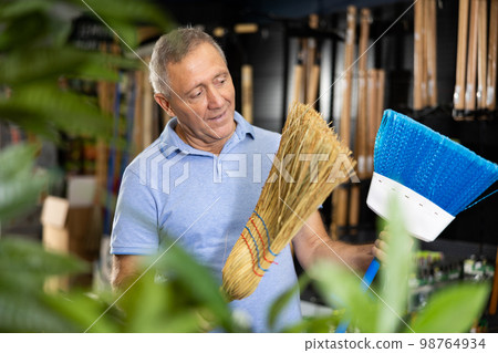 Man choosing broom in household store 98764934