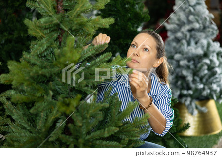 Woman is buying artificial Christmas tree in shop 98764937