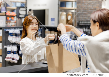 Apparel clerk handing products to customers at the cash register Apparel clerk handing products to customers at the cash register 98770030