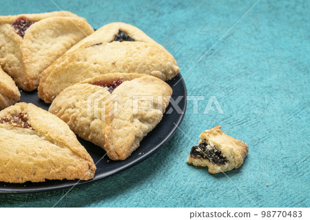 hamantaschen pastry with apricot, raspberry and prune filling on a black ceramic plate, Ashkenazi Jewish cuisine 98770483