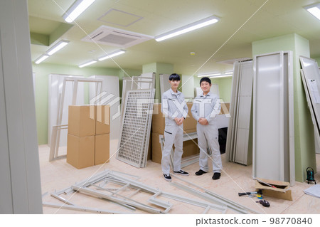 Portrait of two young men in work clothes standing indoors in an apartment building under construction Portrait of two young men in work clothes standing indoors in an apartment building under construction 98770840