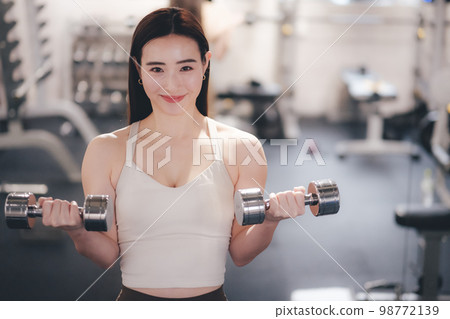 Woman holding dumbbells in both hands at the gym Woman holding dumbbells in both hands at the gym 98772139