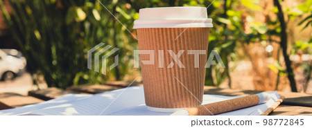 Eco recycling paper cup with coffee or tea on kraft paper with empty paper notebook on wooden bench. Concept of study work outdoors. Take away coffee to go. Copy space for text. Disposable Cardboard Eco recycling paper cup with coffee or tea on kraft paper with empty paper notebook on wooden bench. Concept of study work outdoors. Take away coffee to go. Copy space for text. Disposable Cardboard 98772845