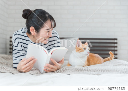 Asian woman playing with pet cat in bedroom at home (reading/skinship) 98774585