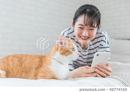 Asian woman playing with pet cat taking pictures with smartphone in bedroom at home 98774589