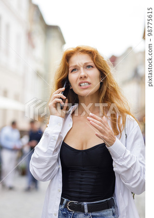 Young redhead woman talking on the phone with anger and stress solving some problems Young redhead woman talking on the phone with anger and stress solving some problems 98775615