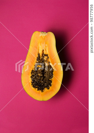 Ripe juicy papaya fruit cut in half on a pink background 98777956