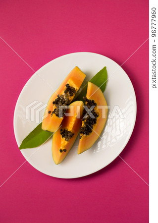 juicy papaya cut into pieces in a plate on a pink Viva Magenta color background 98777960