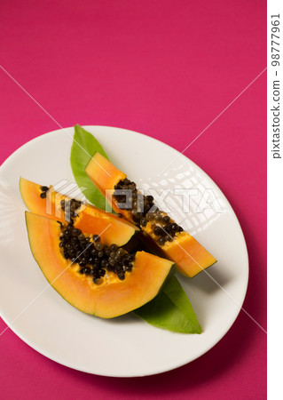 Fresh papaya cut into pieces in a plate on a pink Viva Magenta color background Fresh papaya cut into pieces in a plate on a pink Viva Magenta color background 98777961