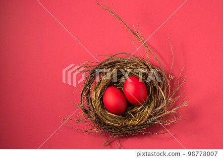 red eggs in a small nest on a pink background 98778007