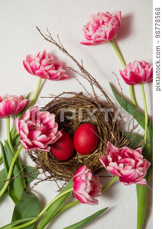 A nest with painted eggs is decorated with beautiful pink tulips on a white background A nest with painted eggs is decorated with beautiful pink tulips on a white background 98778568