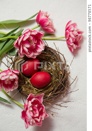 A nest with painted eggs is decorated with pink tulips on a white background A nest with painted eggs is decorated with pink tulips on a white background 98778571