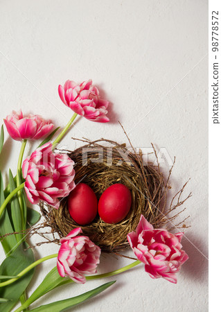 A nest with eggs is decorated with beautiful tulips on a white background A nest with eggs is decorated with beautiful tulips on a white background 98778572