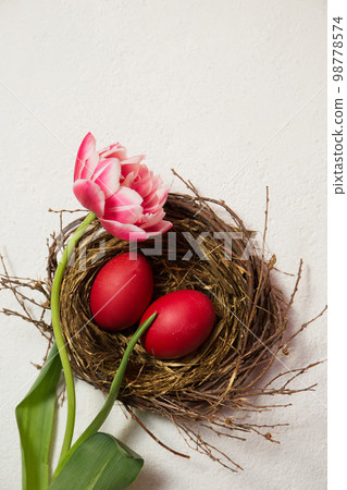 A nest with painted eggs is decorated with beautiful pink tulip A nest with painted eggs is decorated with beautiful pink tulip 98778574