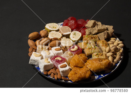 A large plate of various oriental sweets and nuts on a dark 98778580