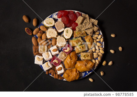 A large plate of various oriental sweets and nuts on a dark background, top view A large plate of various oriental sweets and nuts on a dark background, top view 98778585