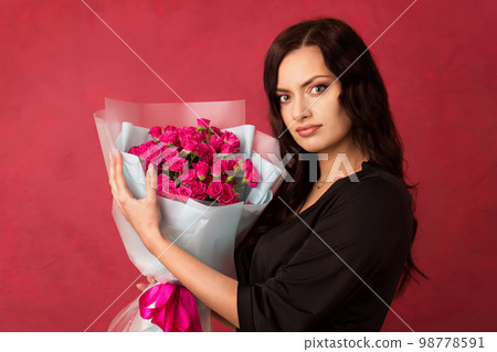 A beautiful young woman is holding a bouquet of pink roses on a pink background A beautiful young woman is holding a bouquet of pink roses on a pink background 98778591