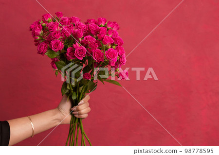 Beautiful bouquet of roses in female hands on a pink background Beautiful bouquet of roses in female hands on a pink background 98778595