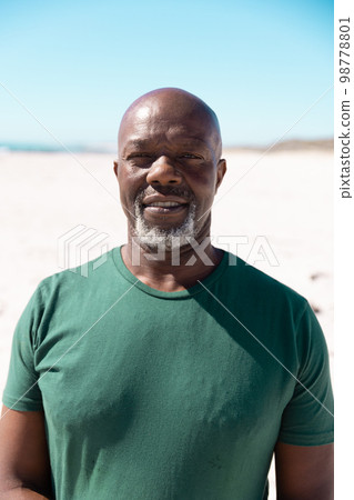 Portrait of bald african american senior man standing on sandy beach against clear blue sky 98778801