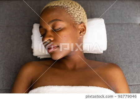 Happy african american woman lying on towel with eyes closed 98779046