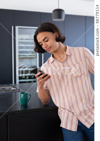 Happy biracial man using smartphone in kitchen Happy biracial man using smartphone in kitchen 98779114
