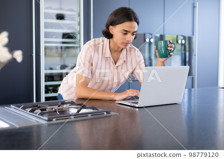 Happy biracial man using laptop in kitchen 98779120