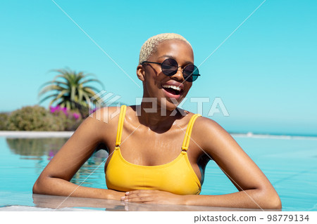 Portrait of happy african american woman wearing sunglasses in swimming pool Portrait of happy african american woman wearing sunglasses in swimming pool 98779134