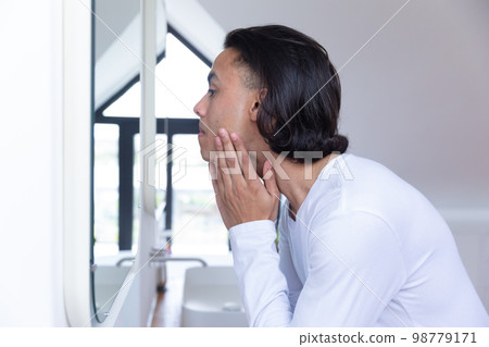 Biracial man looking in mirror in bathroom Biracial man looking in mirror in bathroom 98779171