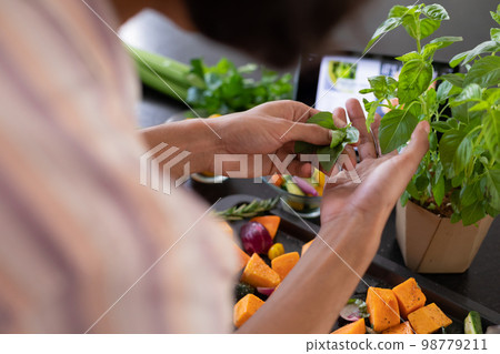 Midsection of biracial man cooking, seasoning vegetables in kitchen 98779211
