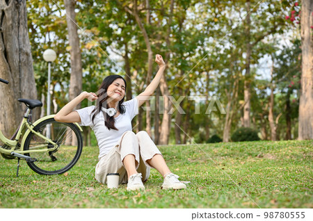 Chilling young Asian woman stretching hands, sitting on grass, relaxing in the park after cycling. Chilling young Asian woman stretching hands, sitting on grass, relaxing in the park after cycling. 98780555