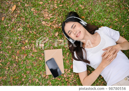 Relaxed and chilling young Asian woman listening to music , smiling, eyes closed and lying on grass Relaxed and chilling young Asian woman listening to music , smiling, eyes closed and lying on grass 98780556