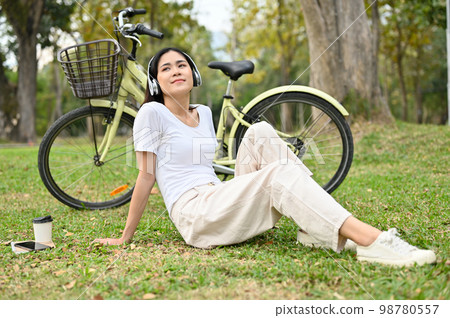 Relaxed Asian woman listening to music and taking a rest after cycling in the public park. 98780557