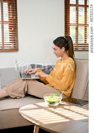 rear view, Beautiful Asian businesswoman using laptop on sofa in her living room rear view, Beautiful Asian businesswoman using laptop on sofa in her living room 98783174