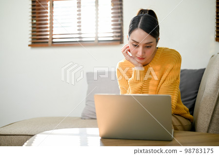 Attractive Asian woman remote working at home, focusing on her tasks on laptop Attractive Asian woman remote working at home, focusing on her tasks on laptop 98783175
